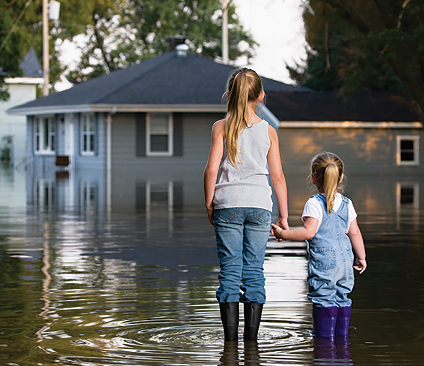 woman and child standing in flooded street in front of house